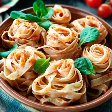 A bowl of pasta artfully twisted into rose-like shapes elegantly topped with rich tomato sauce and garnished with fresh green basil leaves